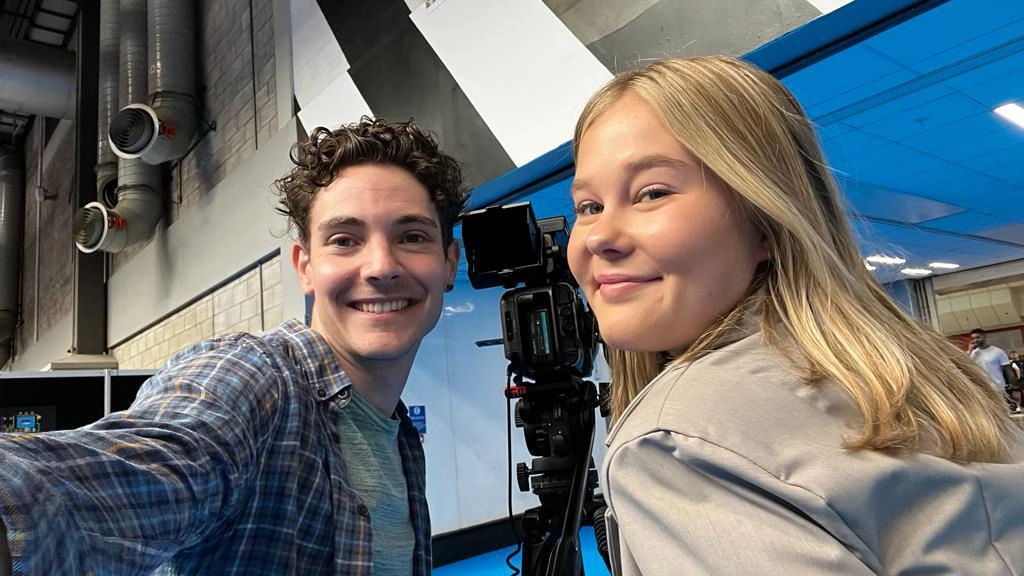 Two film and tv production apprentices taking a selfie next to a professional video camera at the NEC.