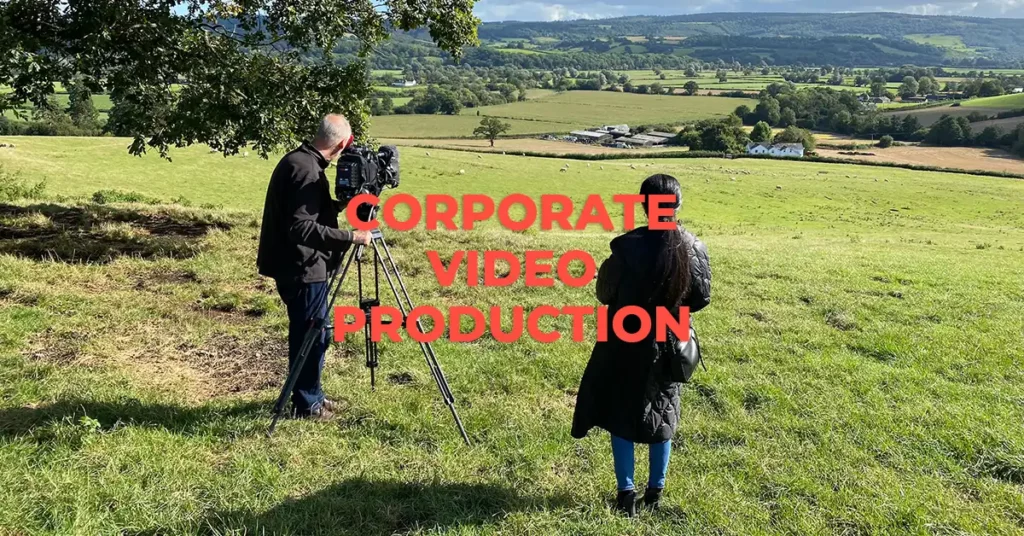 A man and a woman standing in a beautiful green field filming a corporate video.